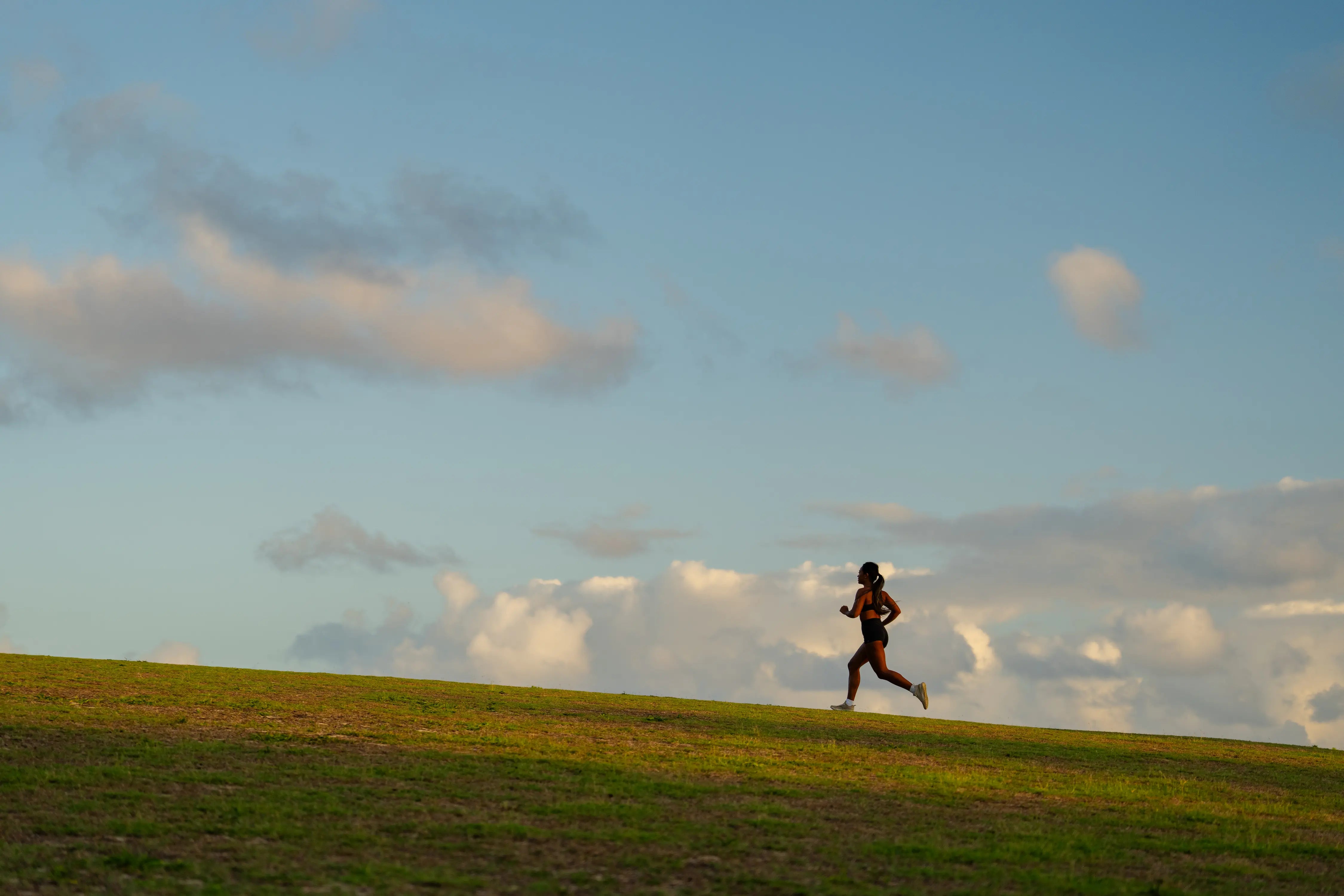 Person running on a grassy field with a blue sky and clouds in the background